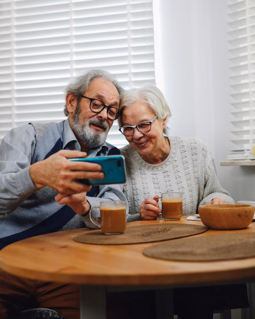 An older couple at a table, looking at a phone together.